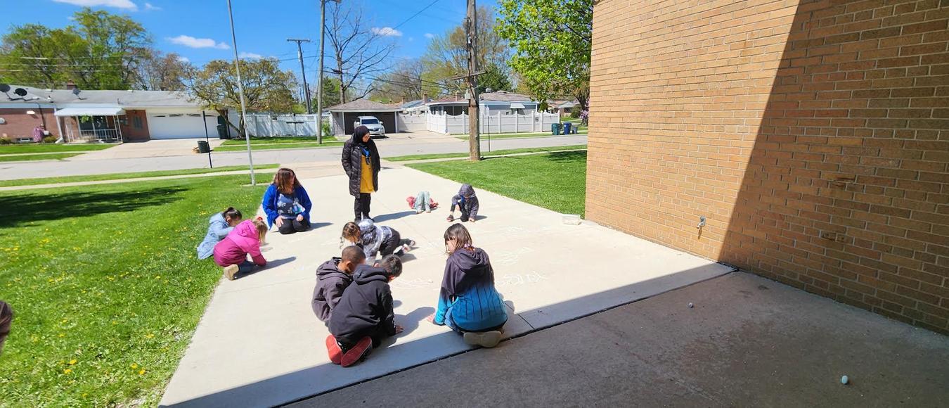 Children are outside drawing on the sidewalk with chalk.