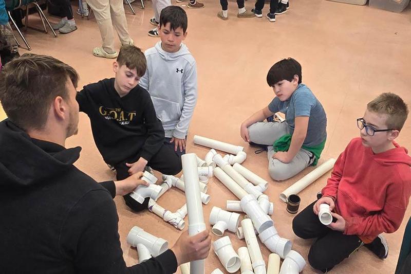 A construction trades student demonstrates how to assemble pipes of various sizes to move sewage and water waste