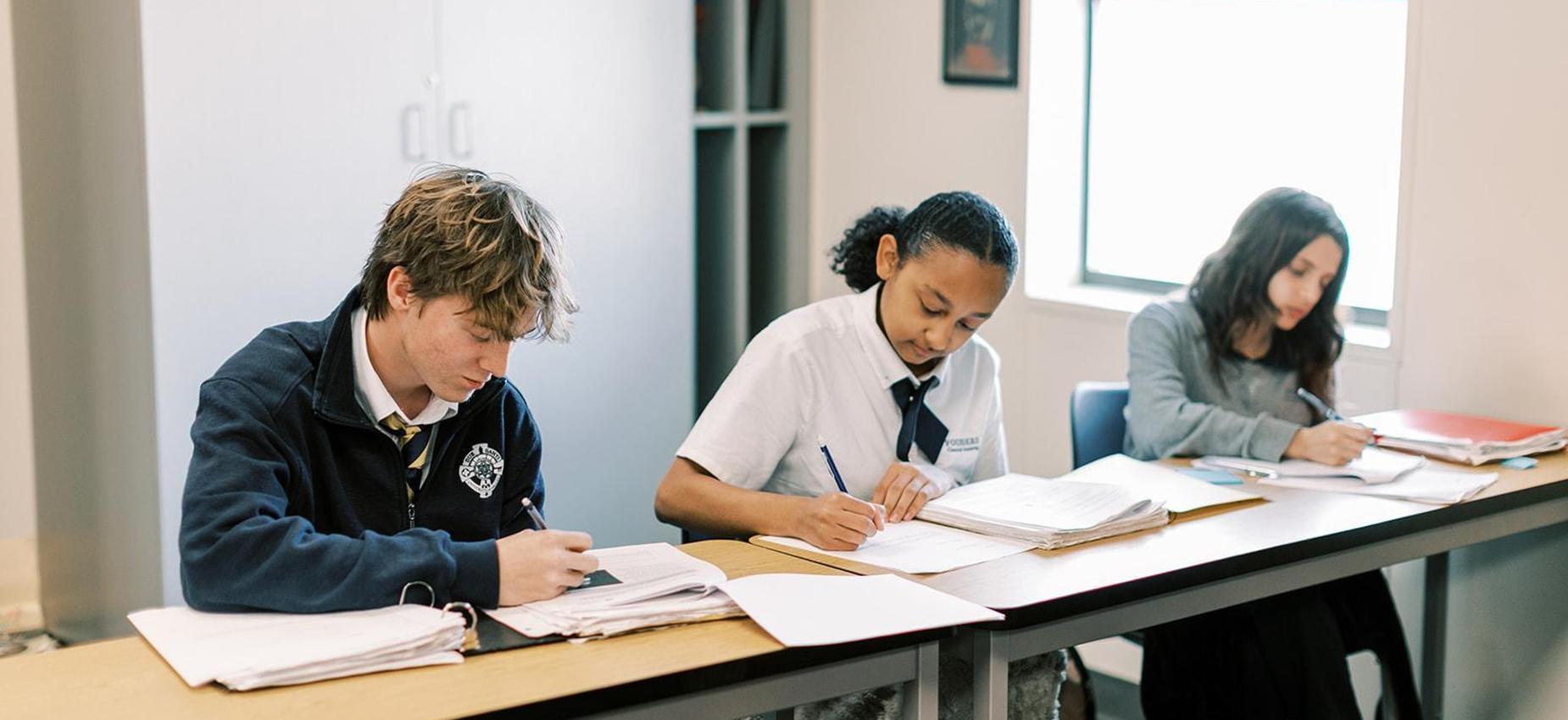 Three upper school students write at their desks during class