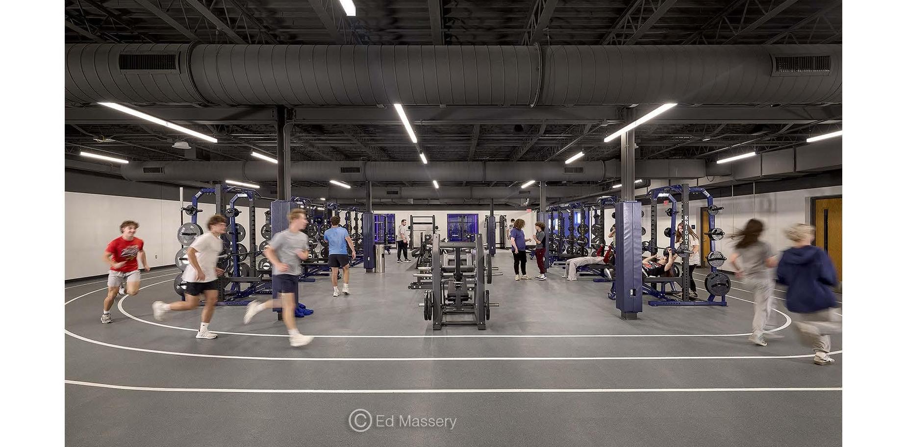 Busy gym with students exercising, various workout stations, and a running track.