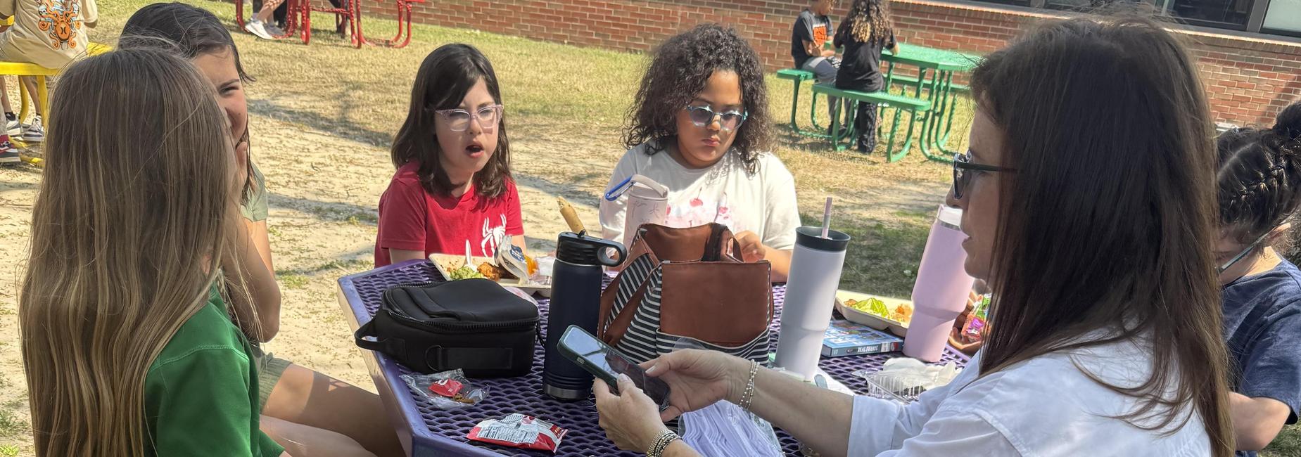 Two people at a purple picnic table with others nearby, enjoying an outdoor activity.