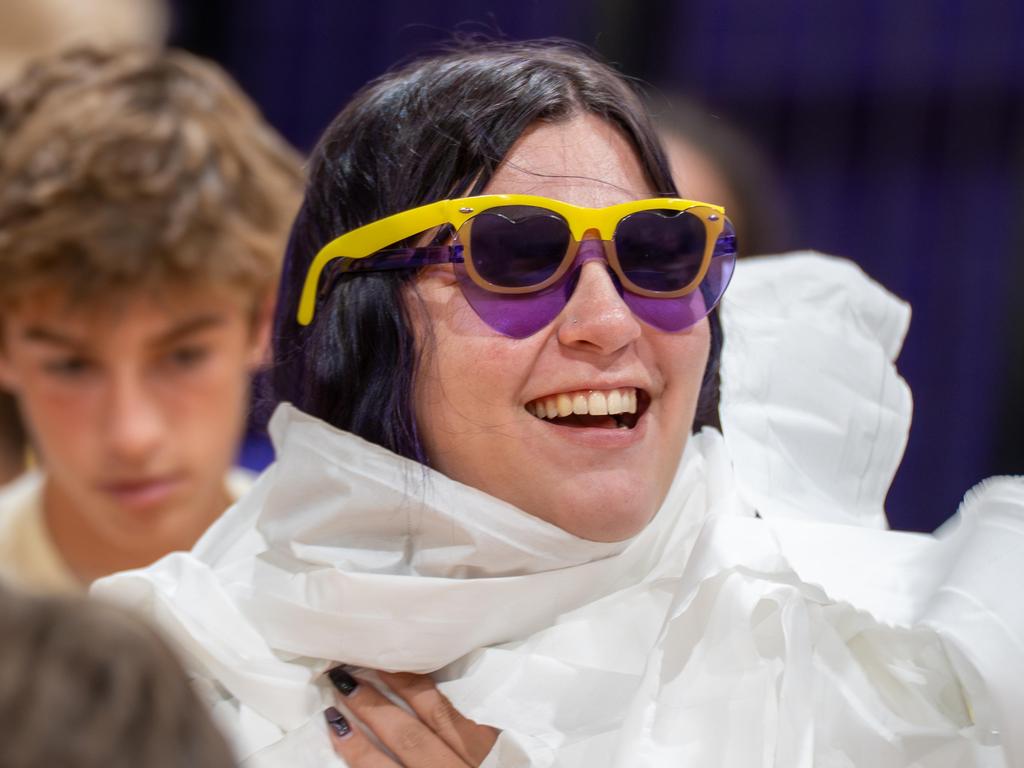 A teacher at a pep rally wearing yellow and purple sunglasses and wrapped in toilet paper.