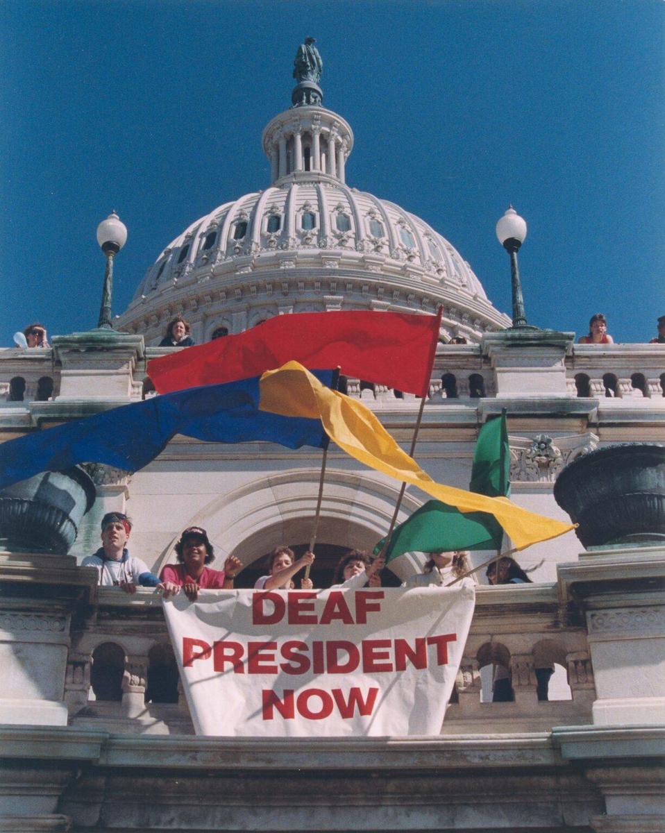 Students protesting in front of capital building holding banner that says deaf president now