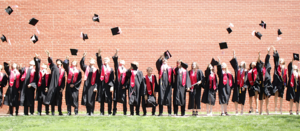 Graduating class throwing caps in the air against a brick wall.