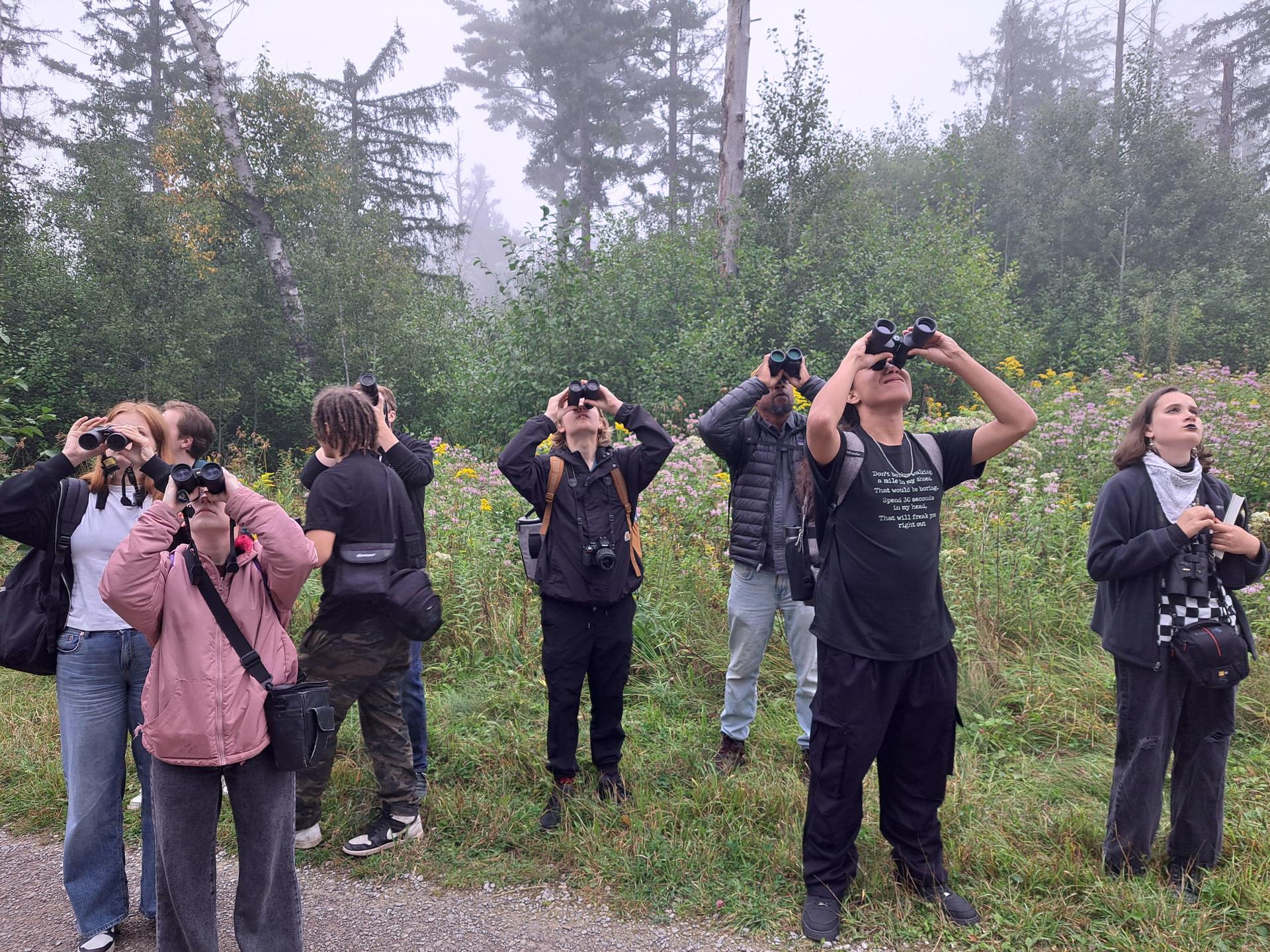 Students looking upwards with binoculars on their faces, looking for birds.
