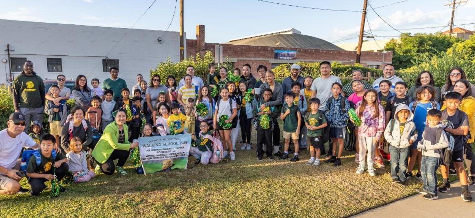 A large group of children and adults gathered outside with a welcome banner.
