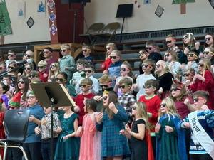 Children in sunglasses sing joyfully, dressed in festive outfits, during a performance.