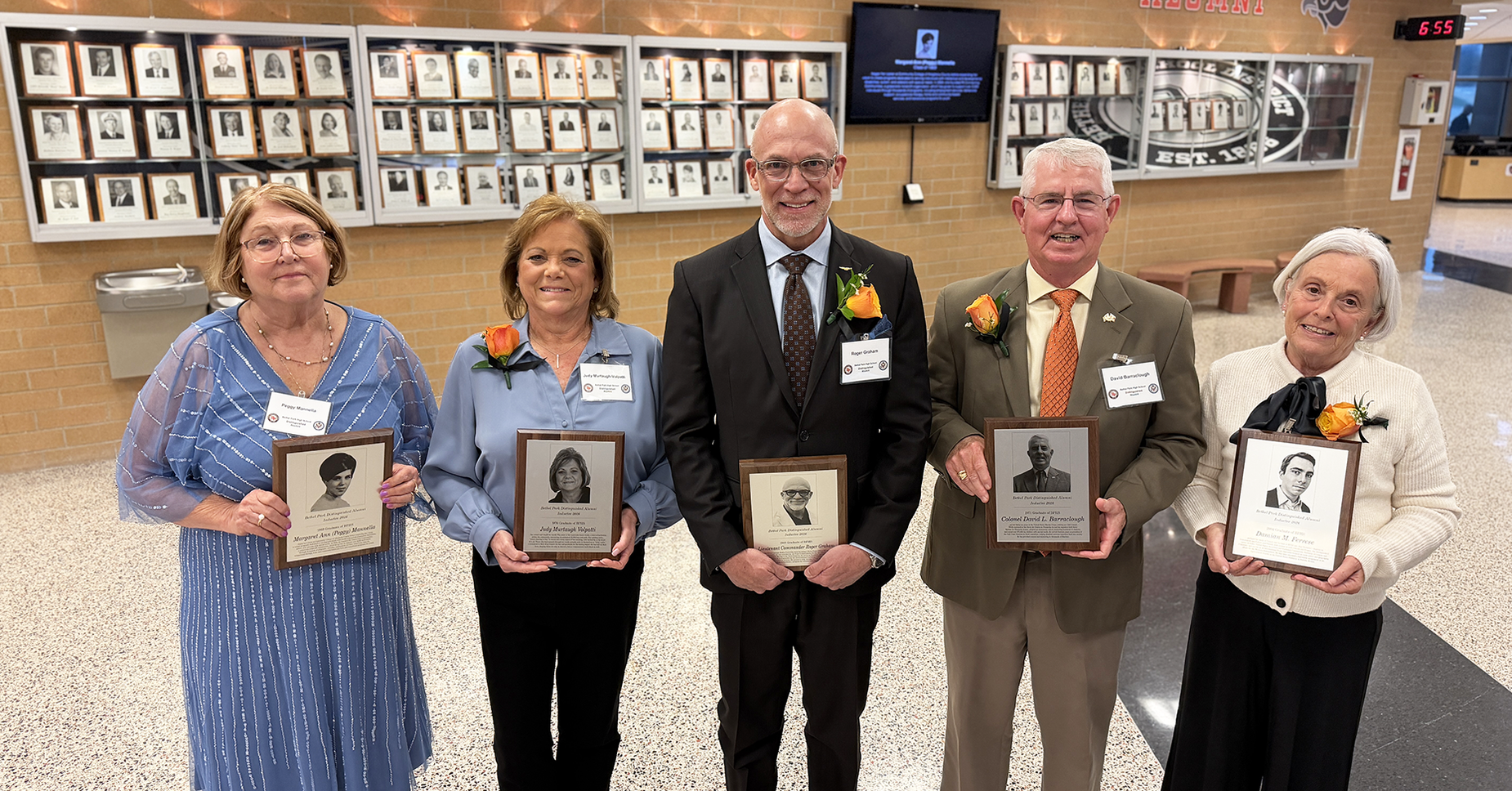 Bethel Park announced ints 2026 Distinguished Alumni. Here they are holding plaques, standing in a hall with framed photos on the wall.