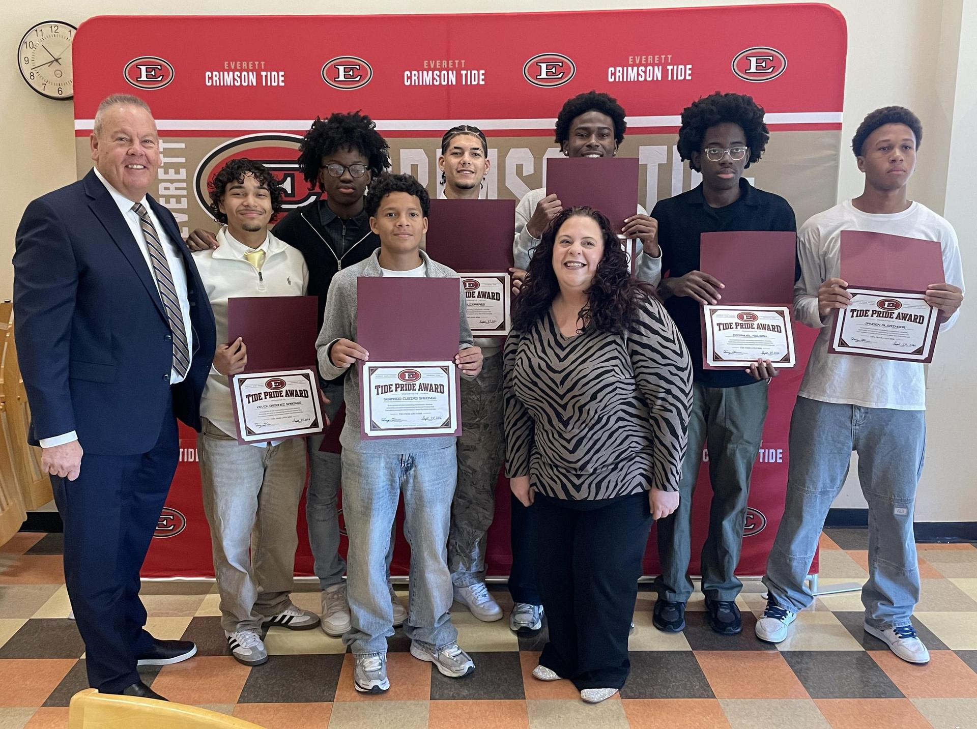 Group of students and adults posing with awards in front of a crimson backdrop.