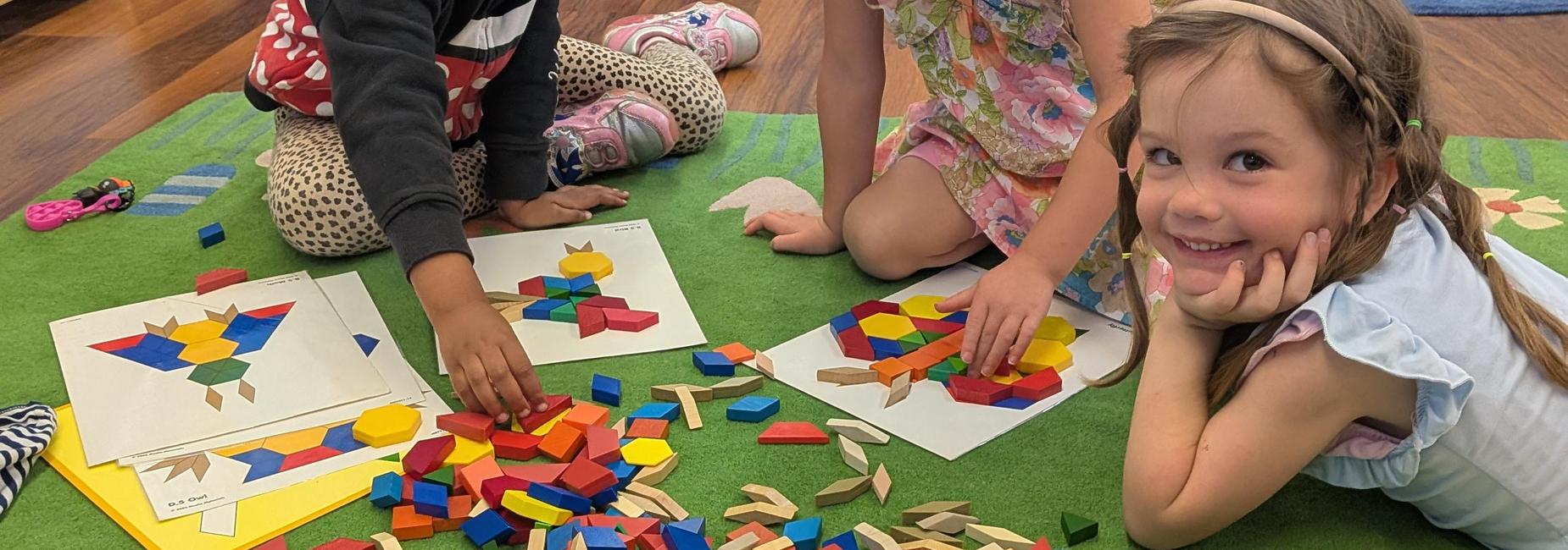 Three kids play with pattern blocks on the rug.