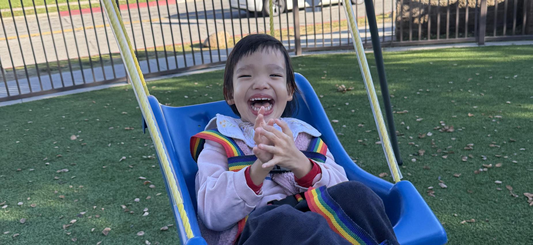 Child joyfully swinging in a playground with a smile and colorful attire.