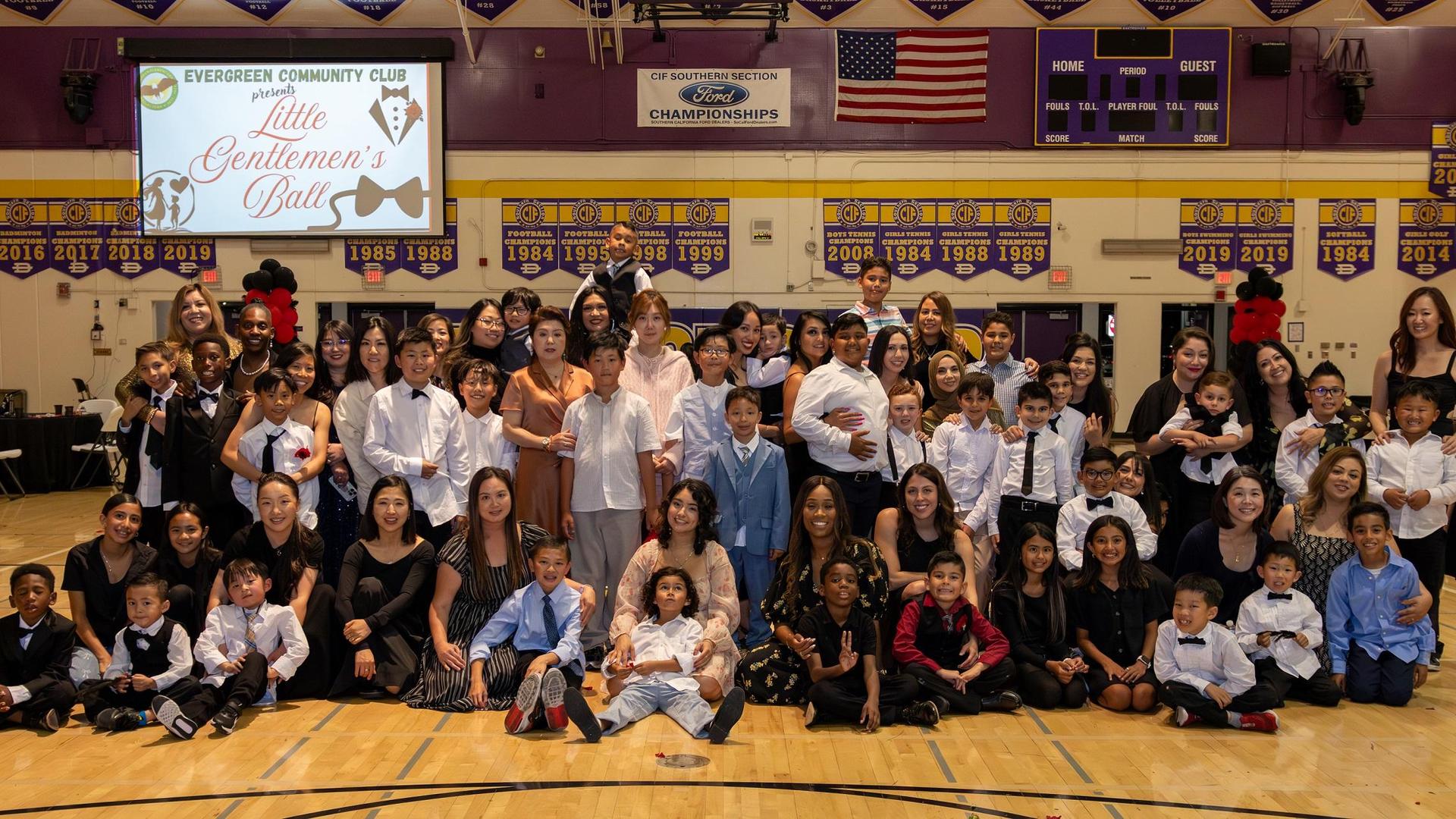 Group of children and adults posing together in formal attire at an event.