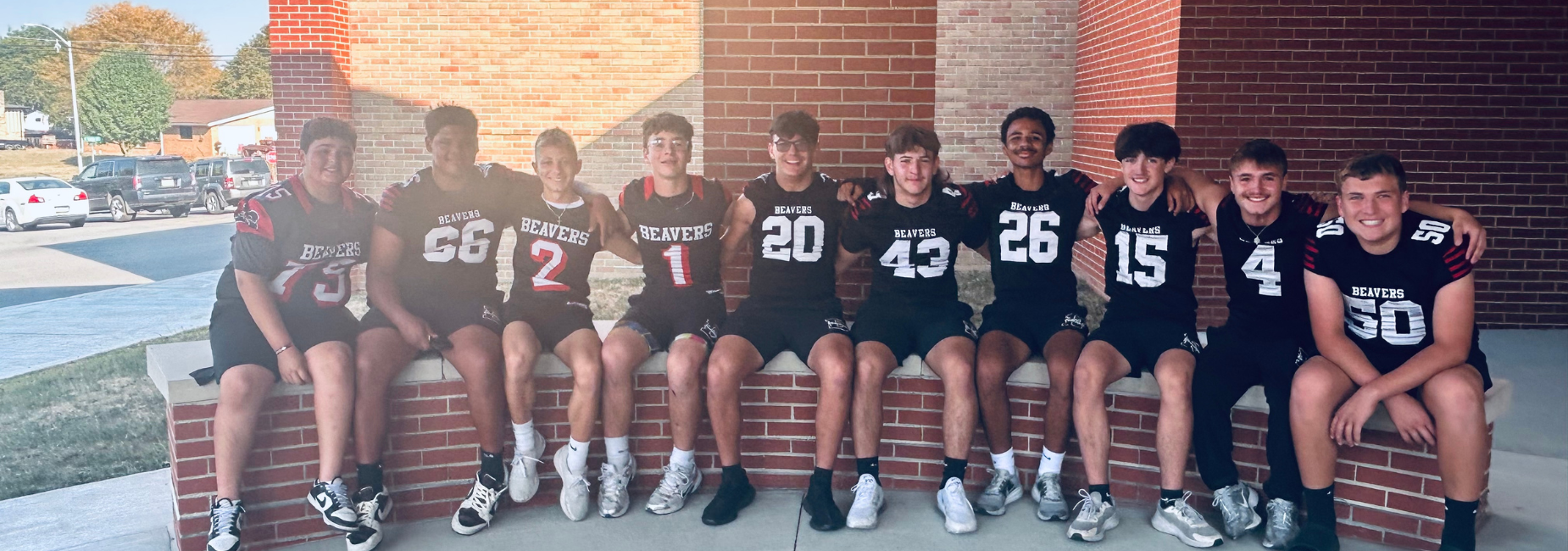 Group of football players posing together on a brick ledge outside.
