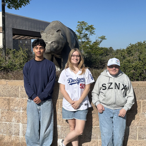 Three Golden Valley High School students pose in front of a grizzly bear statue.