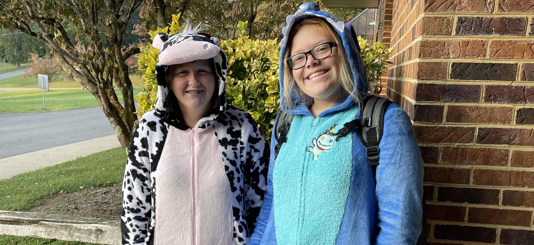 Two students wear pajamas outside a school.