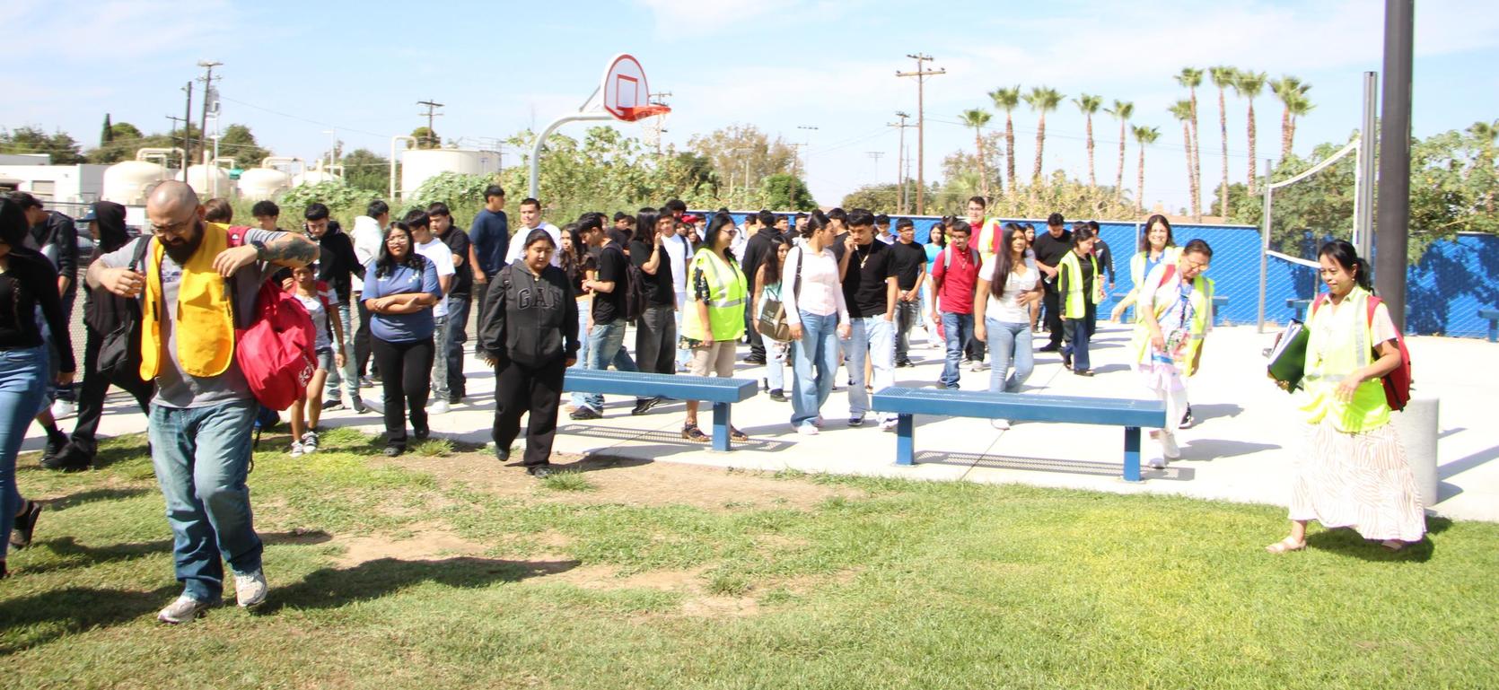 A group of people wearing safety vests walking in an outdoor area with palm trees.