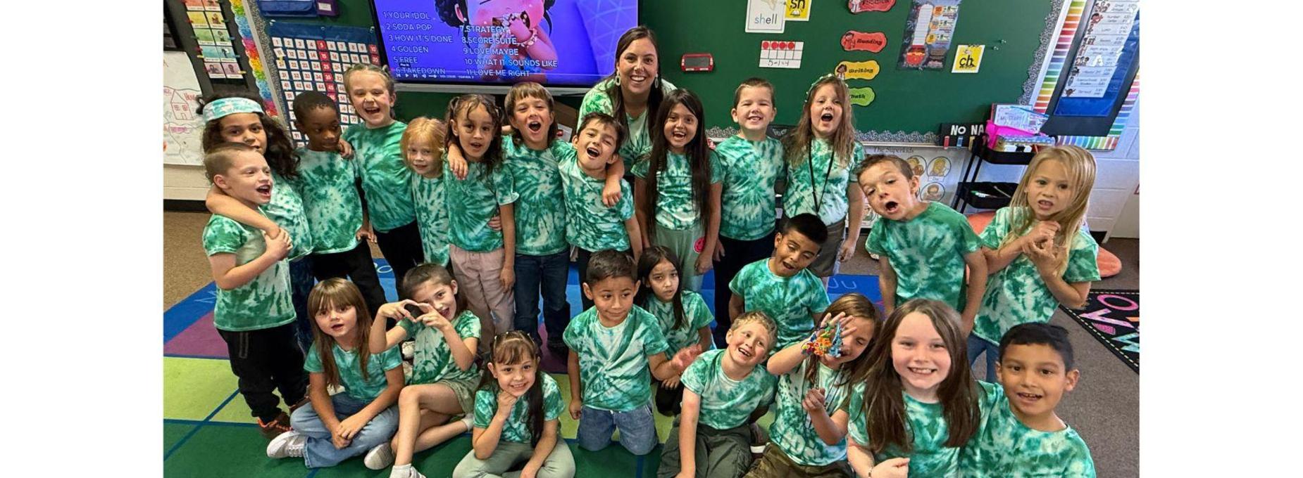 BES students wearing matching tie-dye shirts posing joyfully with their teacher.