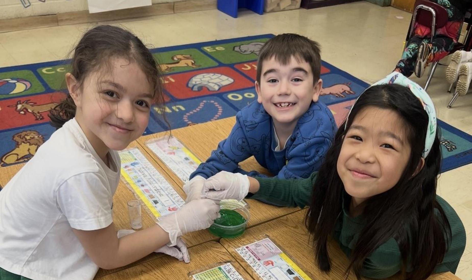 Three children in a classroom experimenting with green liquid.