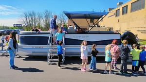 Students climb onto and gather around a pontoon boat outside Penn Yan Elementary School.