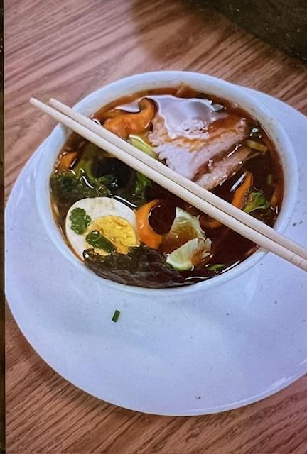 Bowl of soup with vegetables, egg, and chopsticks.