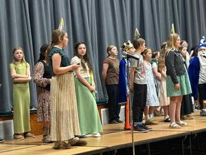 Children in costumes standing on stage with a microphone.