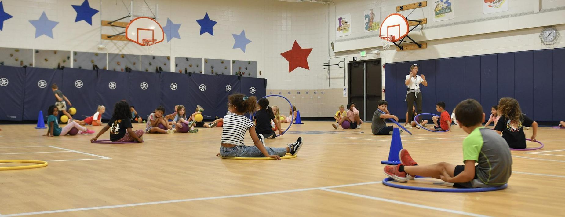 elementary students sitting on the ground in gym class