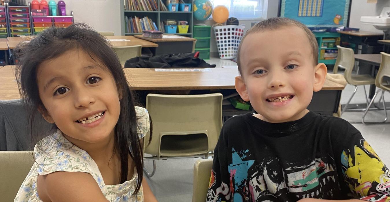 A girl and a boy smiling at the camera while seated at a table.