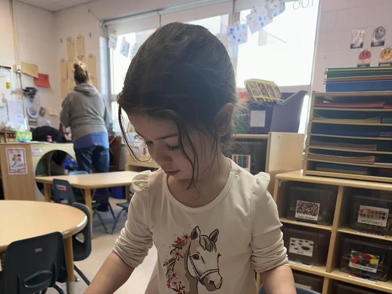 A girl prints with a stamp on paper at a craft table in a classroom.