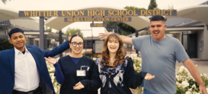 Four USEC students smile and stand in front of the school building.