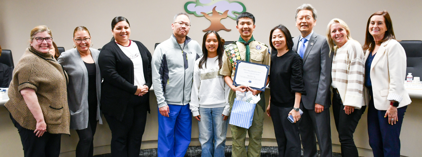 A young boy in a scout uniform receiving an award with family and community members.