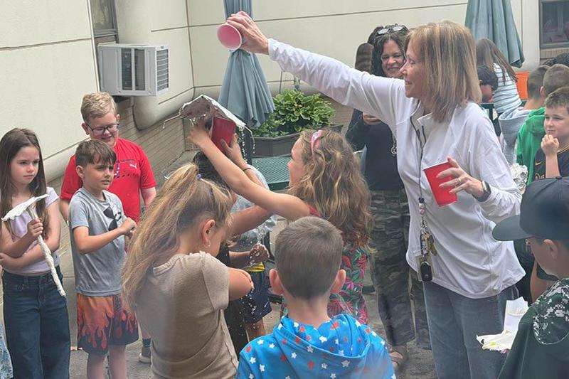 Harrison Park Elementary teacher, Mrs. Kelly Pratt, tests out a student's umbrella by dumping water over her head