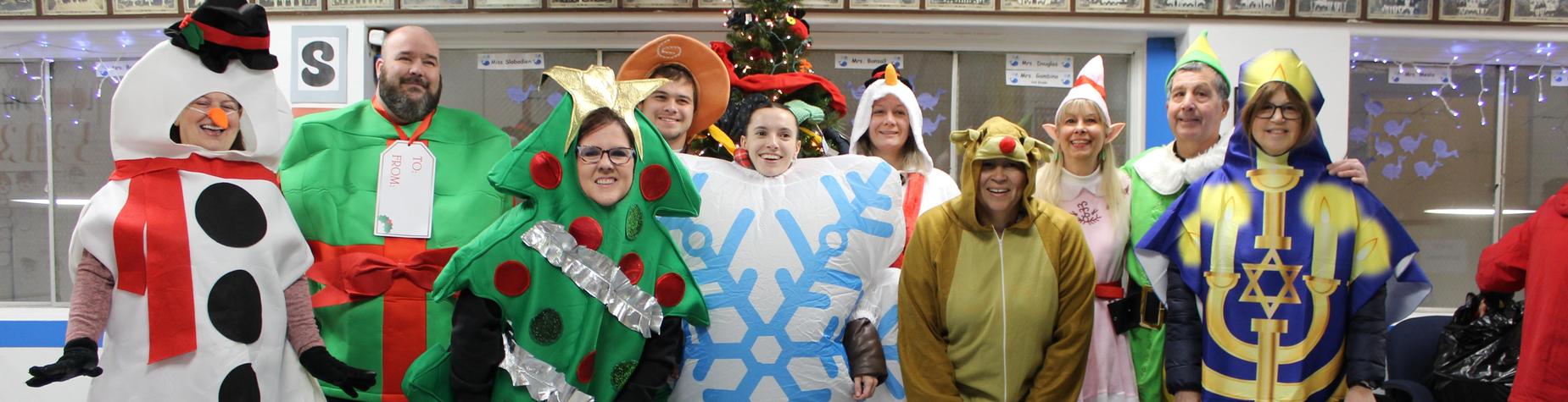 Group of adults in holiday-themed costumes including trees, snowflakes, and animals, smiling together.