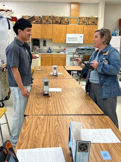 A woman showing a presentation to a student at a table in a classroom.