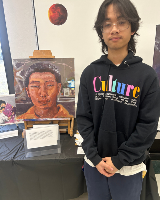 Another student stands in front of artwork display