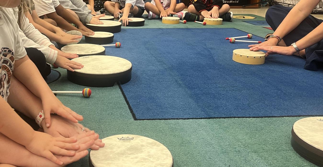 Children playing hand drums in a classroom setting.