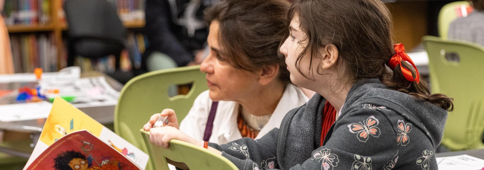 An elementary student and her mother read a book together at a literacy event