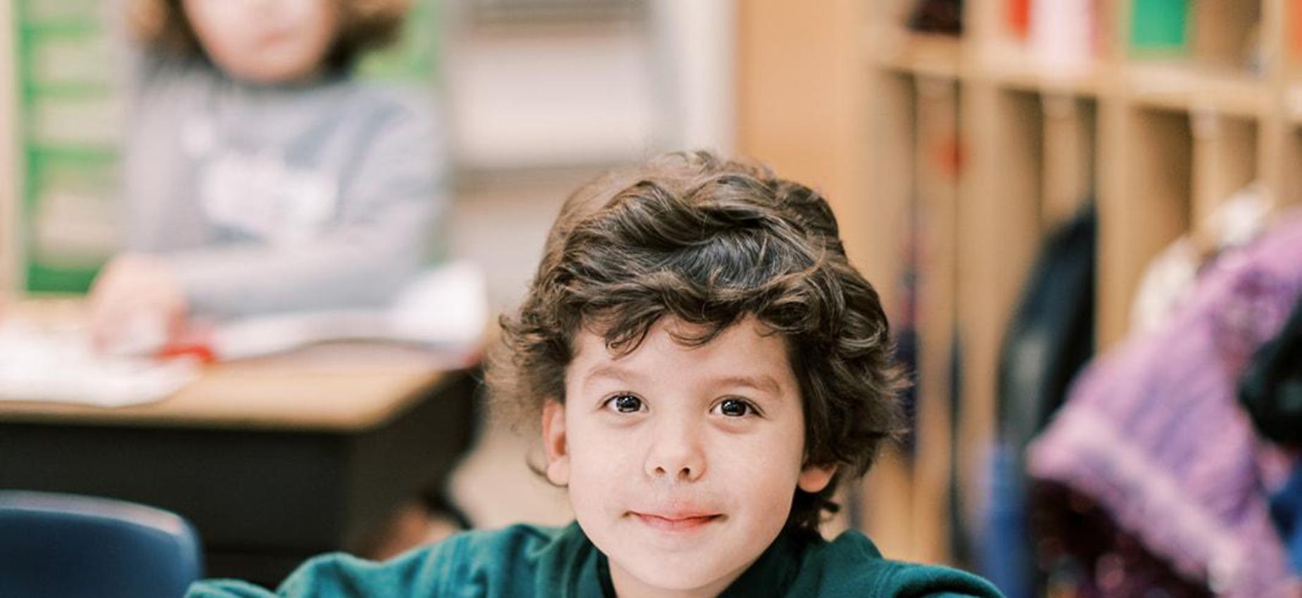 Smiling elementary student sits at his desk with an open book