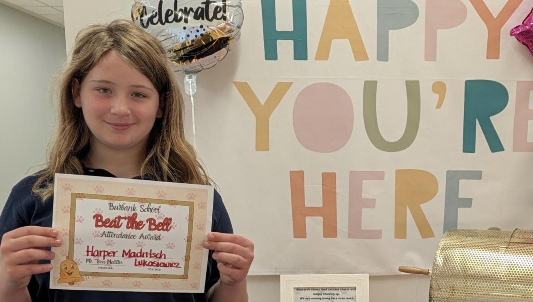 Child holding a certificate in front of a celebratory banner.