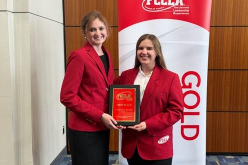 Two high school students atnading in front of a red bannder holding a plaque