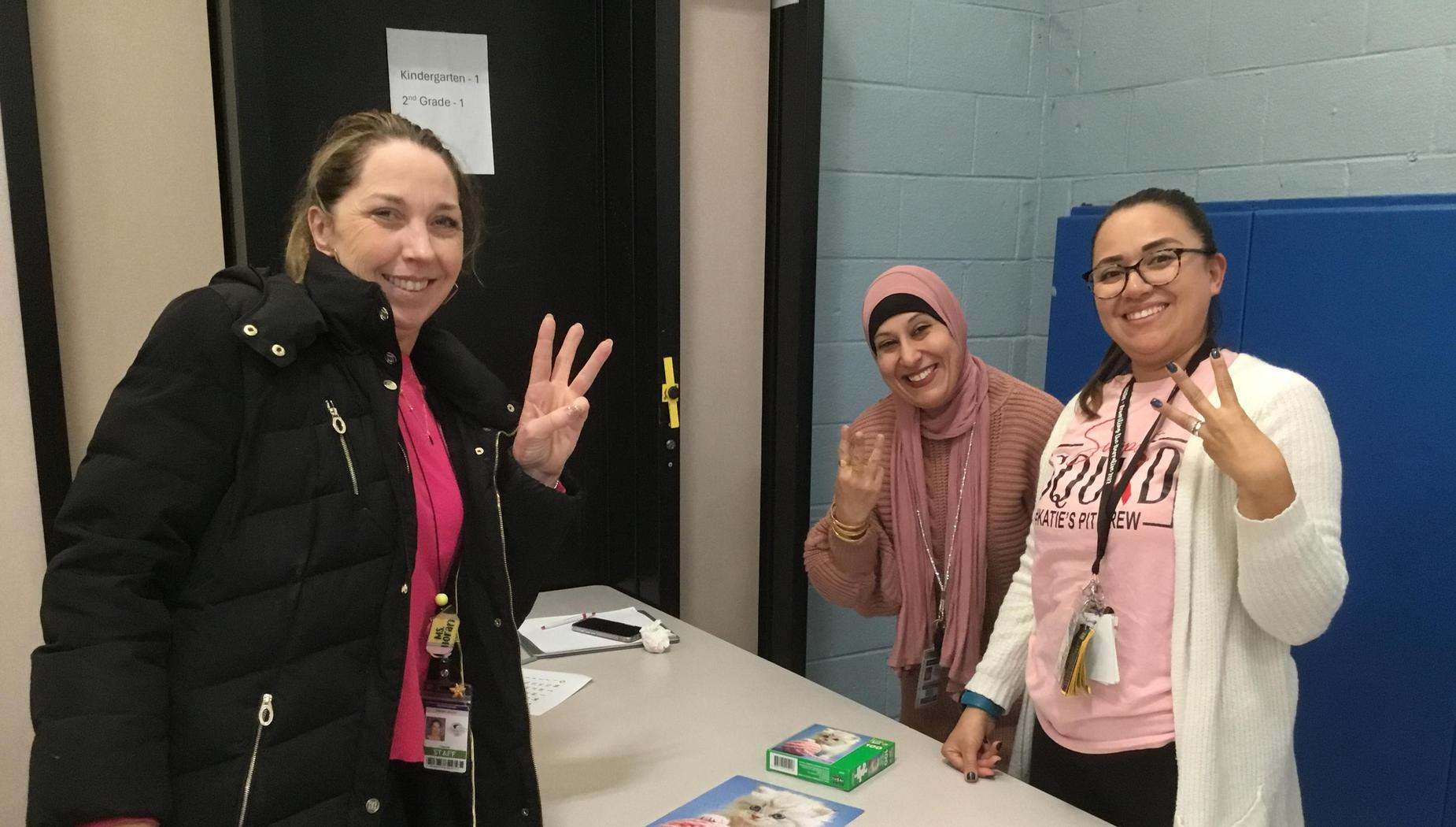 Three women showing peace signs next to a colorful puzzle on a table.