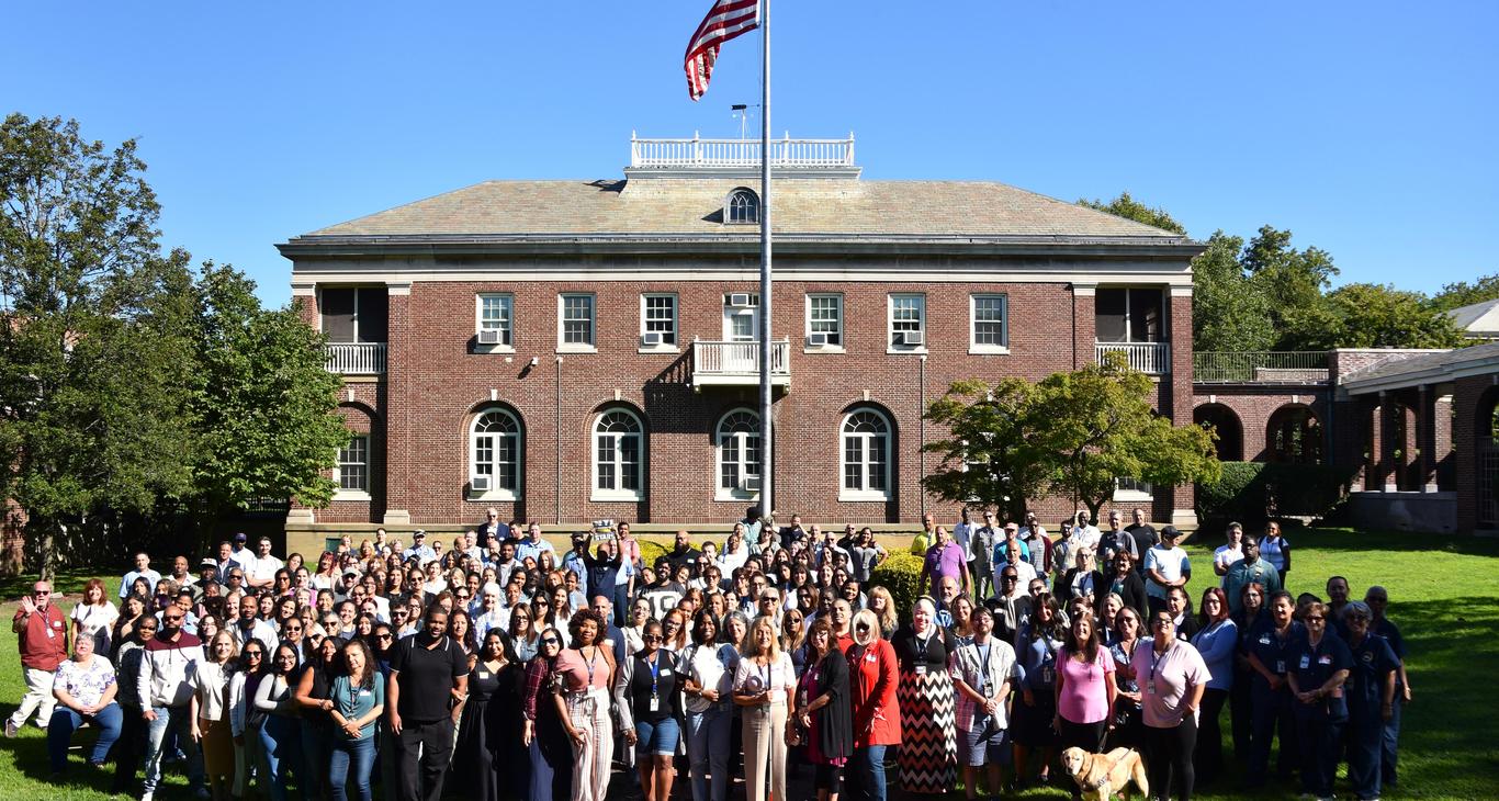 A large group of people gathered outside a brick building with an American flag.