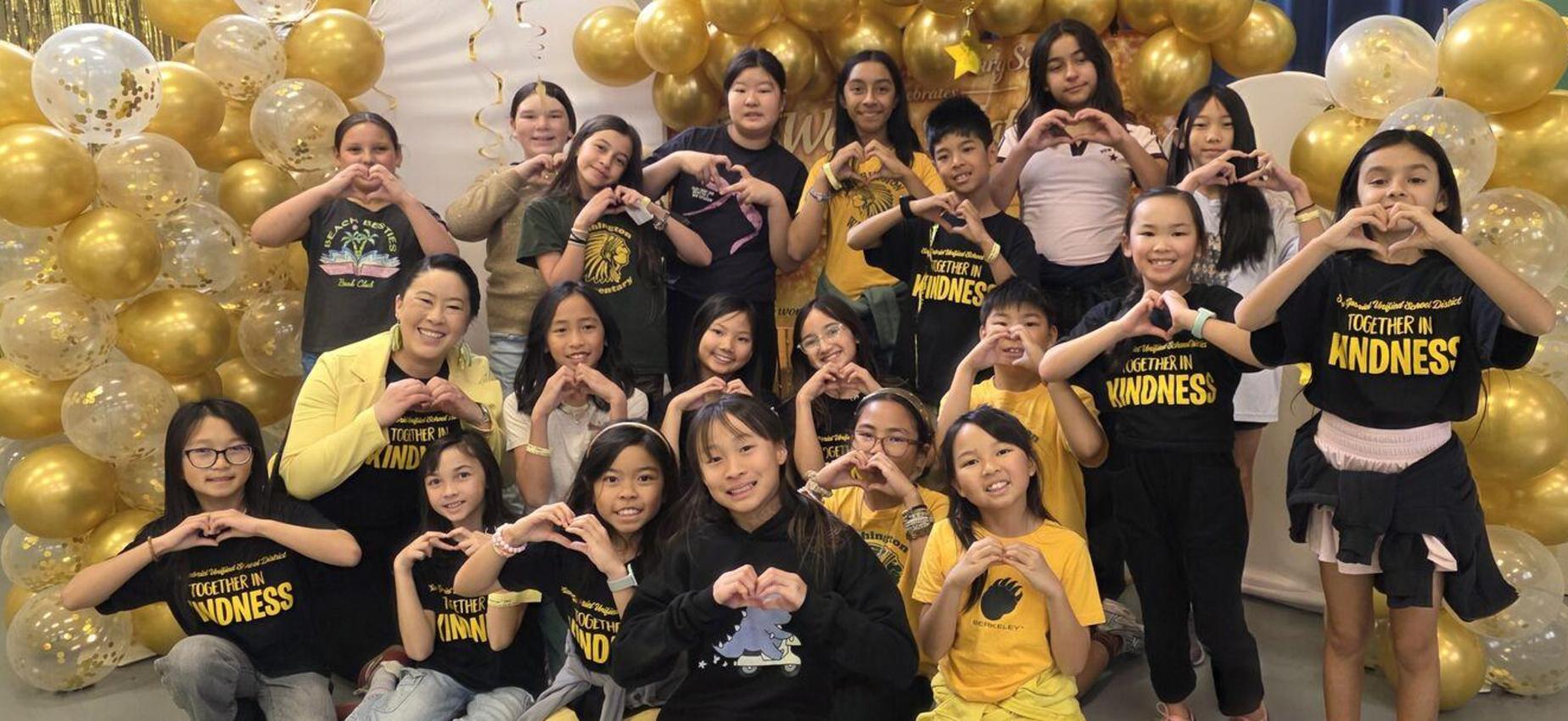 Group of children forming hearts with their hands in a festive setting.