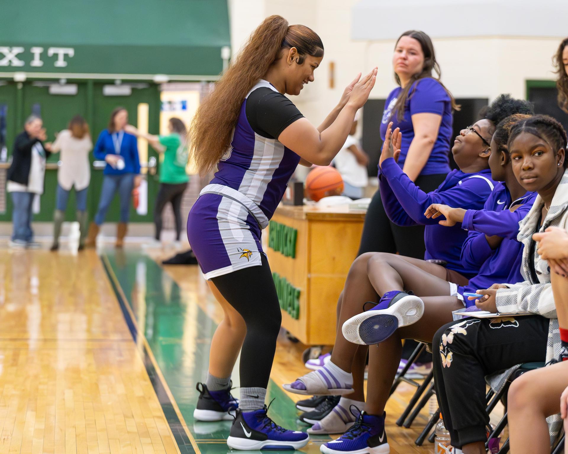 Two varsity girls basketball players slapping hands while on the sidelines..