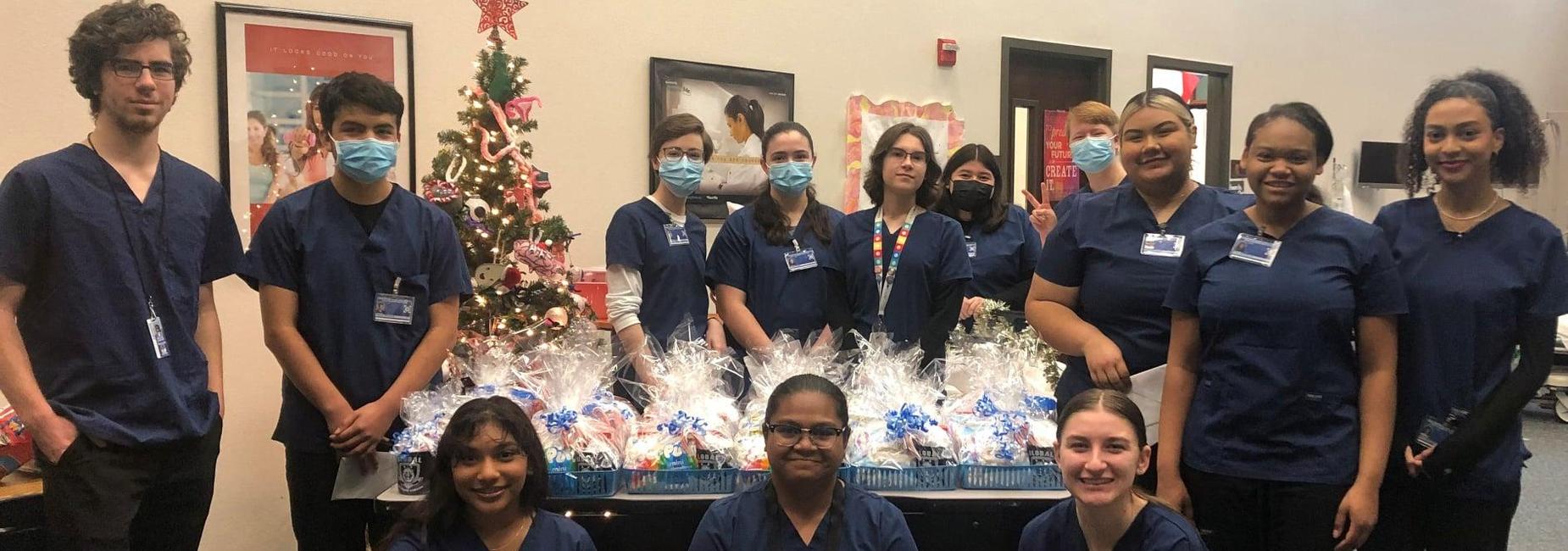 teen students in scrubs stand around a table full of gifts