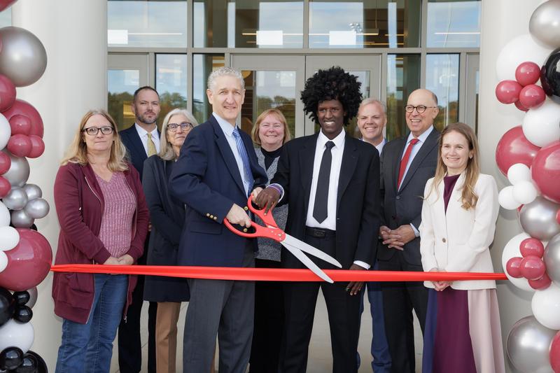 Group of people behind ribbon with large scissors and balloon decor on either side.