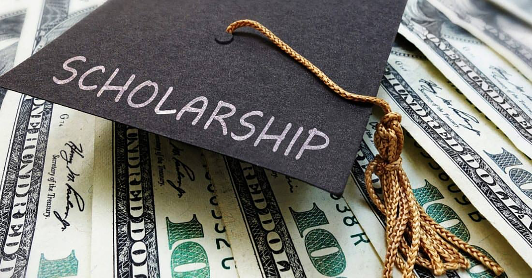 Graduation cap with a scholarship tag on a pile of dollar bills.
