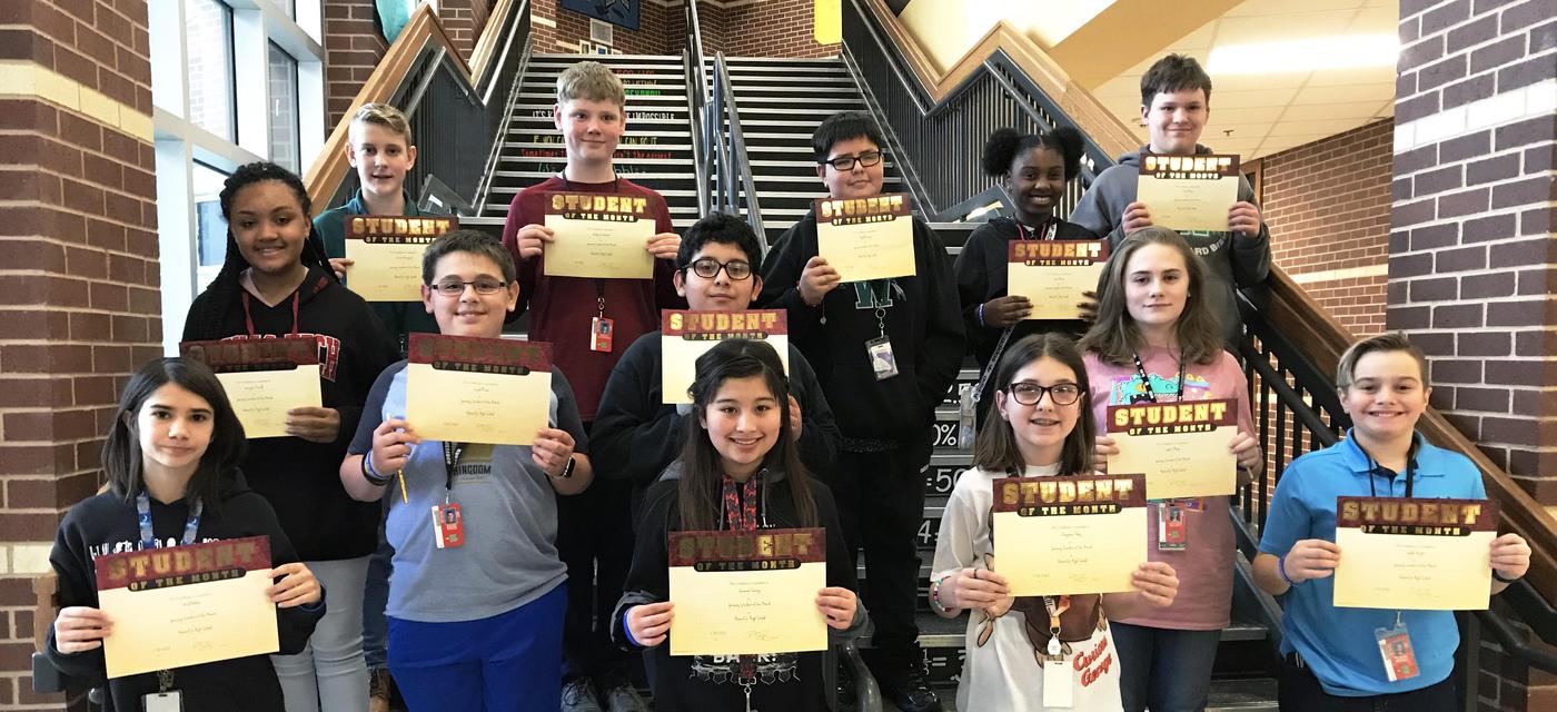 group of 13 students pose on steps with student of the month certificates