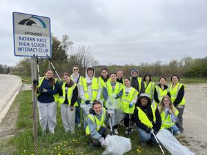 Group of students in yellow vests posing by an "Adopt-A-Highway" sign.