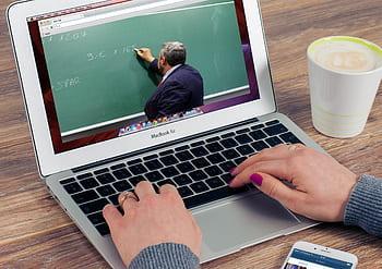 hands typing on laptop showing teacher at chalkboard.