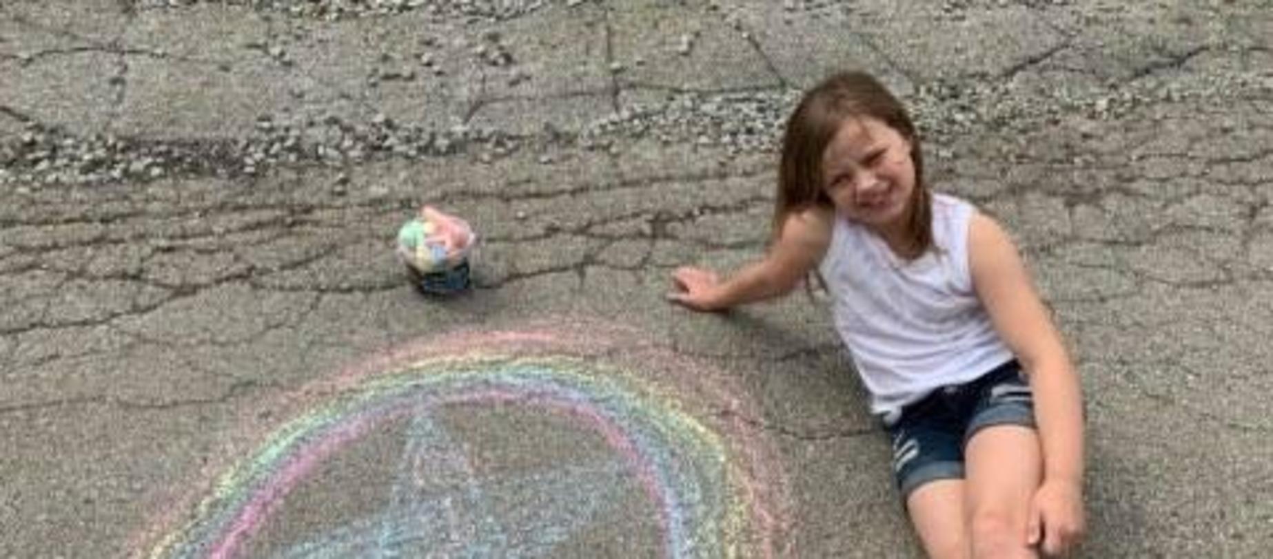 girl sitting on driveway playing with sidewalk chalk